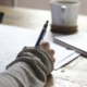 person writing on brown wooden table near white ceramic mug