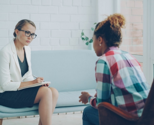 Clinician taking notes on a clipboard while a client speaks during a behavioral health intake assessment