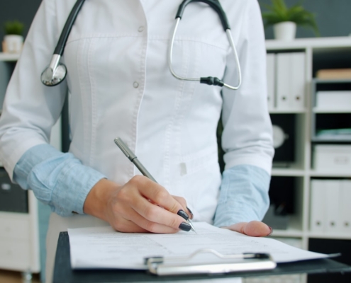 Clinician completing continued stay review documentation on a clipboard in an office lined with patient record binders