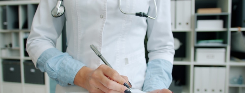Clinician completing continued stay review documentation on a clipboard in an office lined with patient record binders